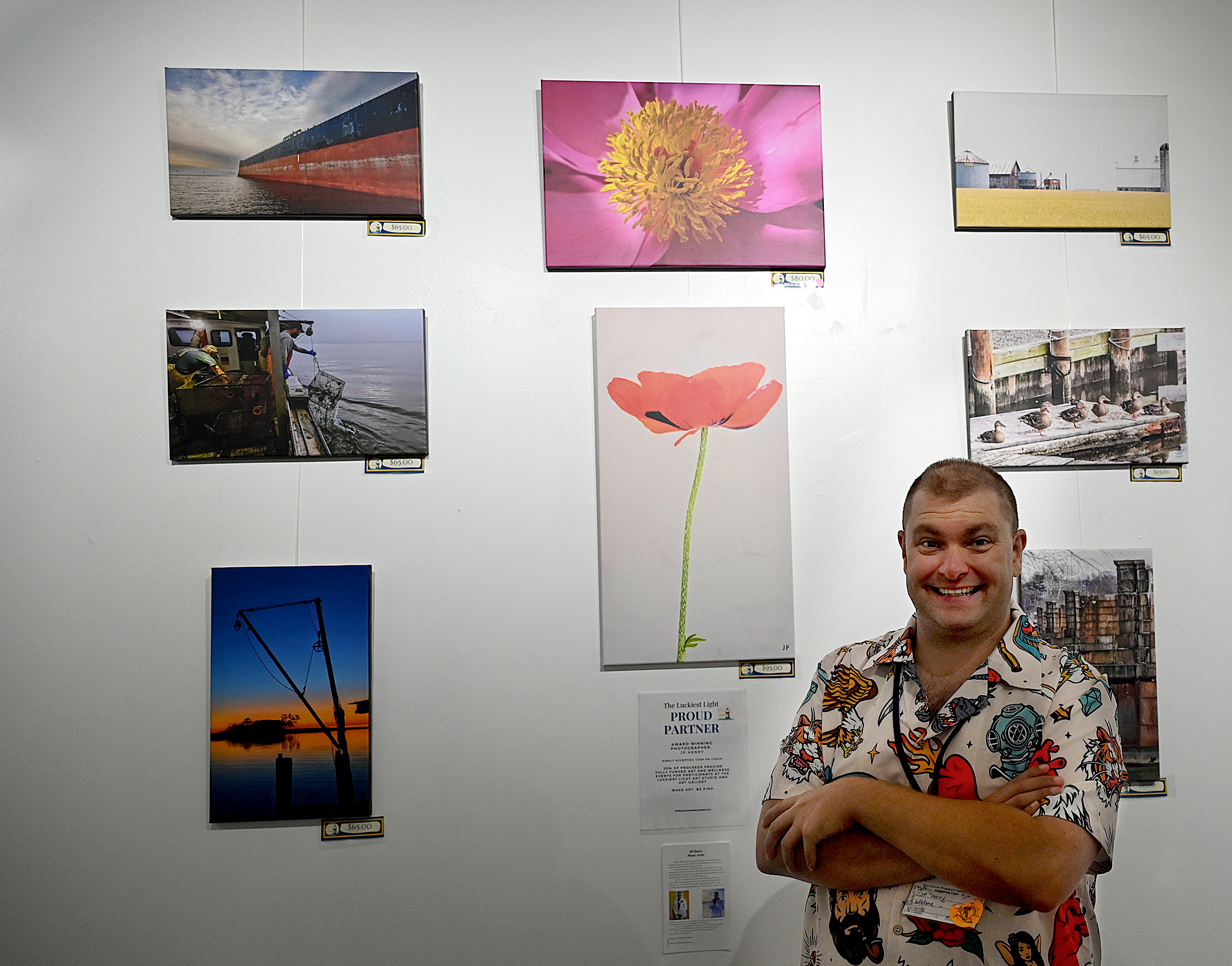 Photographer JP Henry stands in front of his photographs hanging...