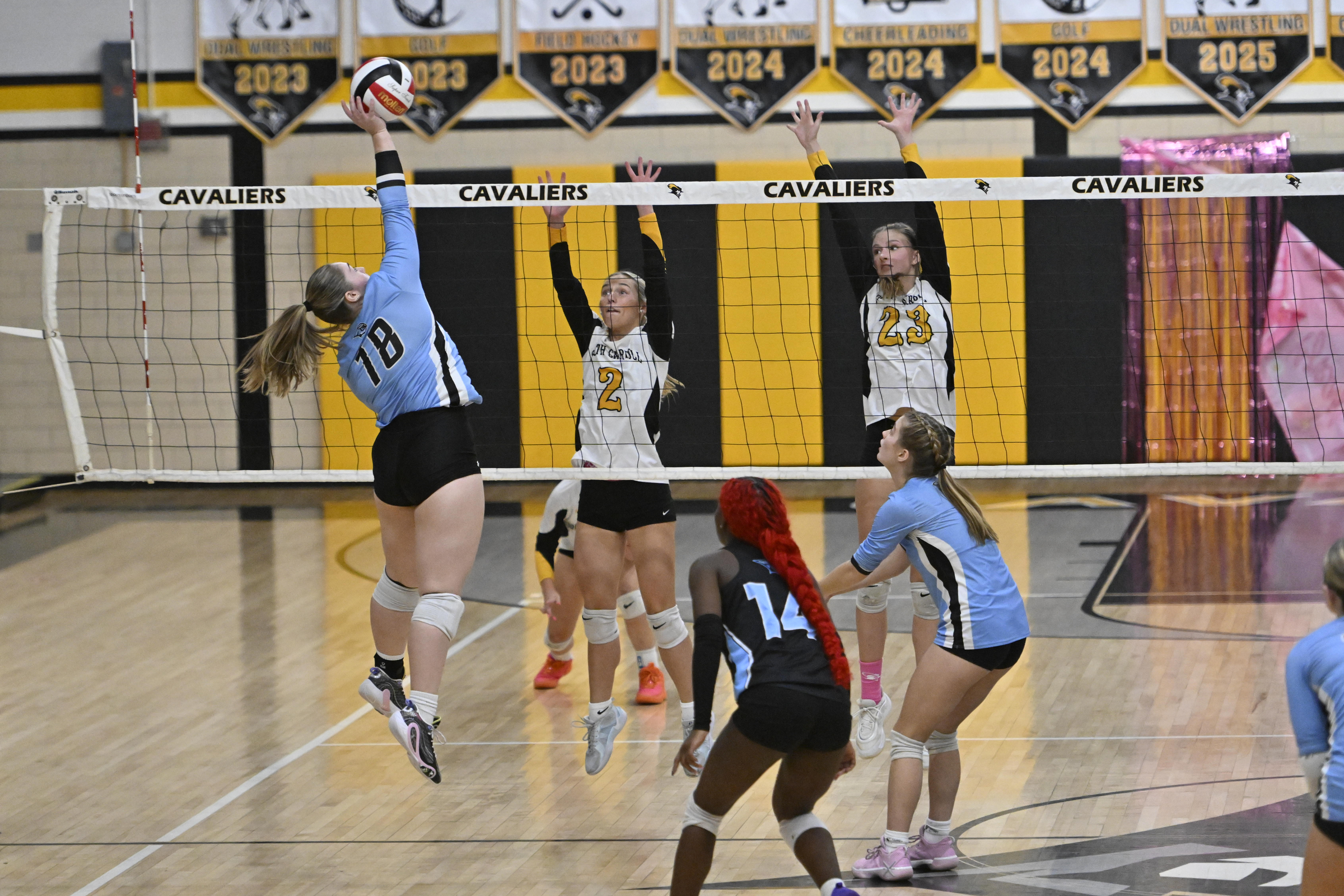 Keira Sniffen spikes the ball as Erin Taylor, left, and...